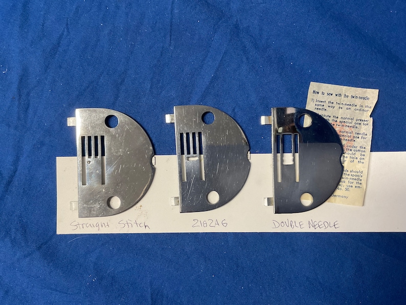 Peut inclure: Trois plaques &agrave; aiguilles en m&eacute;tal pour machine &agrave; coudre, &eacute;tiquet&eacute;es "Point droit", "216246" et "Double aiguille".