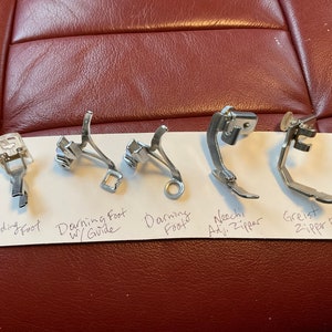 Peut inclure: Cinq pieds de machine &agrave; coudre diff&eacute;rents, dont un pied pour cordon, un pied pour repriser avec guide, un pied pour repriser, un pied pour fermeture &eacute;clair r&eacute;glable Nechi et un pied pour fermeture &eacute;clair Greist.