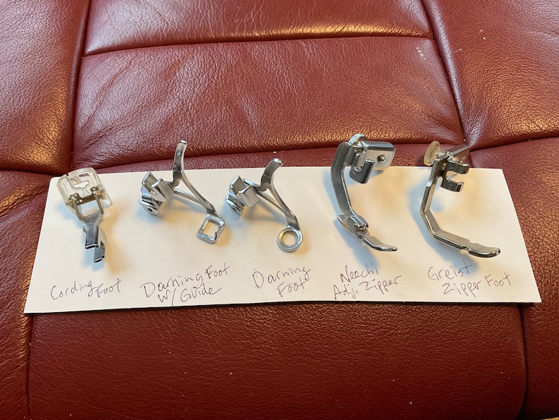 Peut inclure: Cinq pieds de machine &agrave; coudre diff&eacute;rents, dont un pied pour cordon, un pied pour repriser avec guide, un pied pour repriser, un pied pour fermeture &eacute;clair r&eacute;glable Nechi et un pied pour fermeture &eacute;clair Greist.