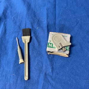 Peut inclure: Un ensemble d'outils de couture comprenant un petit tournevis gris, une brosse grise &agrave; poils noirs et un enfile-aiguille gris dans une bo&icirc;te blanche avec du texte vert qui dit "NEcchi 1 AGHI N. 1".