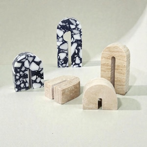 May include: Five arch-shaped decorative objects. Two are black with white speckled patterns, and three are beige stone. The objects vary in size and shape, with a cutout arch design.