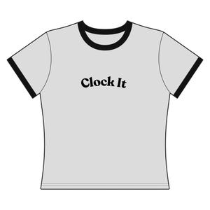 May include: A light gray t-shirt with black trim around the collar and sleeves. The words "Clock It" are printed in black, centered on the front of the shirt. The shirt has a classic, casual style.