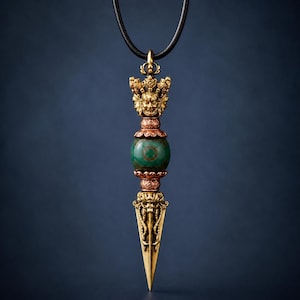 Può includere: Un ciondolo composto da un phurba in metallo dorato con un volto di divinità dettagliato sulla sommità e una lama affilata alla base. Una perla rotonda in pietra verde scuro con un motivo circolare è posizionata tra due distanziatori color rame.