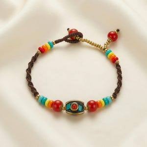 May include: A colorful beaded bracelet with a brown cord. The bracelet features red, orange, yellow, green, and blue beads, along with a central decorative element with a red center. The bracelet is adjustable.