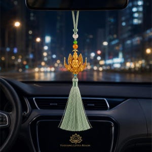 May include: A car rearview mirror hanging ornament featuring a gold-coloured Buddha figure seated on a lotus flower. The ornament includes a light green cord, a pale pink bead, a green bead, an orange bead, and a long light green fabric tassel.