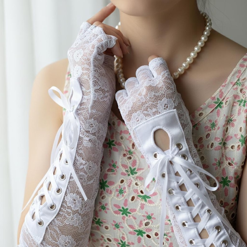 Peut inclure: Gants en dentelle blancs avec un motif floral et des liens en ruban de satin. Les gants sont sans doigts avec une petite ouverture au dos de la main. Les gants sont longs, remontant le long du bras.