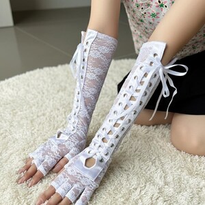 Peut inclure: Gants blancs sans doigts en dentelle avec fermeture &agrave; lacets en satin. Les gants s'&eacute;tendent jusqu'au milieu de l'avant-bras et pr&eacute;sentent un motif de dentelle florale d&eacute;licat. Les gants ont un d&eacute;tail d&eacute;coup&eacute; au niveau des jointures.