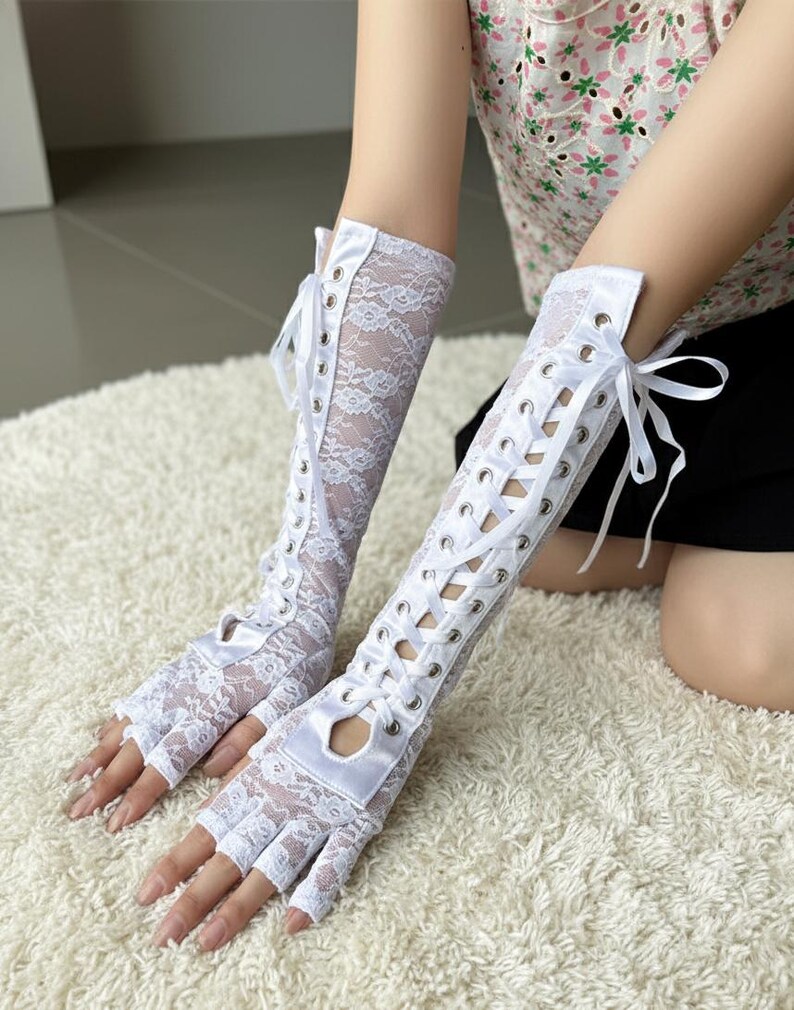 Peut inclure: Gants blancs sans doigts en dentelle avec fermeture &agrave; lacets en satin. Les gants s'&eacute;tendent jusqu'au milieu de l'avant-bras et pr&eacute;sentent un motif de dentelle florale d&eacute;licat. Les gants ont un d&eacute;tail d&eacute;coup&eacute; au niveau des jointures.
