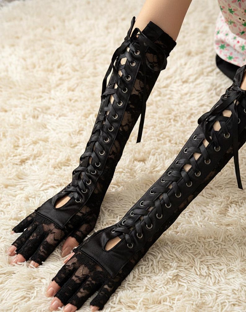 Peut inclure: Gants noirs sans doigts en dentelle avec un panneau en satin et un la&ccedil;age. Les gants remontent le long du bras et pr&eacute;sentent une d&eacute;coupe au niveau des jointures. Esth&eacute;tique gothique ou victorienne.