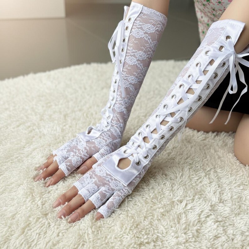 Peut inclure: Gants blancs sans doigts en dentelle avec un motif floral et des liens en ruban de satin. Les gants s'&eacute;tendent jusqu'au coude et comportent des &oelig;illets pour le ruban. Les gants sont en dentelle d&eacute;licate.
