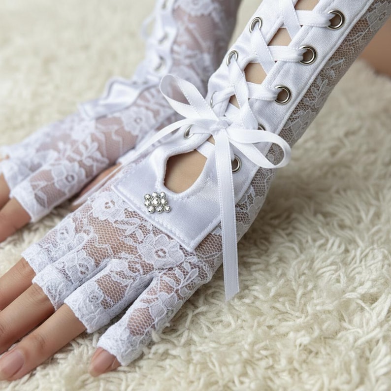 Peut inclure: Gants blancs sans doigts en dentelle avec un motif floral. Les gants ont un poignet en satin avec un n&oelig;ud et un ornement en strass. Les gants ont un la&ccedil;age au dos de la main.