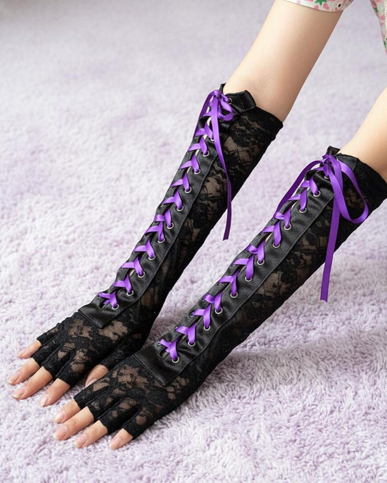 Peut inclure: Gants sans doigts en dentelle noire avec un panneau en satin et un la&ccedil;age en ruban violet. Les gants s'&eacute;tendent jusqu'au coude et pr&eacute;sentent un motif de dentelle florale d&eacute;licate. Un accessoire de mode gothique ou alternatif.