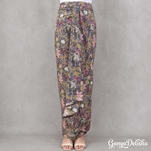 Op de afbeelding: Een enkellange wikkelrok met een donkergrijze basis en een ingewikkeld bloemen-batikpatroon in roze, gele en witte tinten. De rok heeft een recht silhouet met een verticaal voorpaneel en wordt gedragen met sandalen met open tenen.