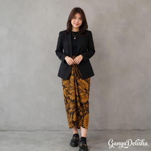 May include: A black blazer worn over a black top and a long skirt featuring a yellow and black floral pattern. The outfit includes black shoes and a gold necklace. The text GanyaDelisha is visible in the bottom right corner of the image.