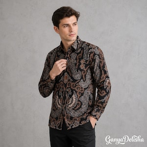 May include: A long-sleeved button-down shirt featuring a black and brown batik pattern with intricate swirling motifs and stylised wing shapes. The shirt has a standard collar, a front button placket, and a consistent repeating design throughout.