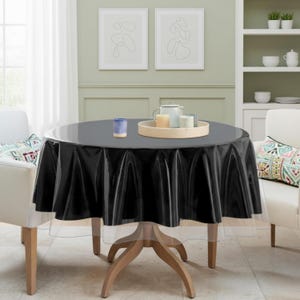 May include: A round black tablecloth with a clear vinyl underlay covers a wooden table. A tray with candles and a teapot sits on the table. Two white armchairs with patterned pillows are on either side of the table.