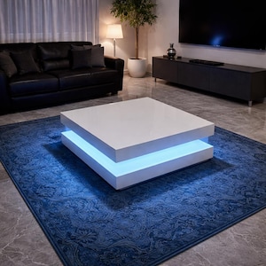 Peut inclure: Une table basse carrée blanche moderne avec une bande lumineuse LED bleue. La table est posée sur un tapis bleu foncé à motifs. Un canapé en cuir noir et un meuble de télévision gris foncé sont en arrière-plan.