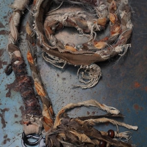 May include: A braided lanyard crafted from strips of fabric in shades of brown, tan, and orange, featuring frayed edges and a fuzzy texture. The lanyard includes a dark metal swivel clasp and a decorative tassel with small brown wooden beads.