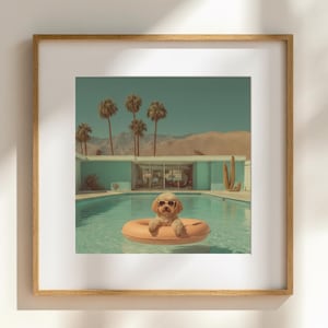 May include: A framed print featuring a dog wearing sunglasses floating in a pool on an orange inflatable ring. The background includes palm trees, a mid-century modern house, and a desert landscape under a clear sky. The image has a vintage, retro aesthetic.
