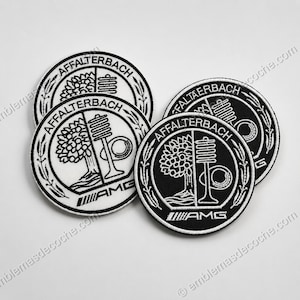 Puede incluir: Tres parches bordados circulares con un diseño en blanco y negro. Cada parche muestra el texto AFFALTERBACH en la parte superior, un gráfico de un árbol y una válvula en el centro, y el logotipo de AMG en la parte inferior, dentro de un borde.