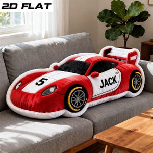 May include: A plush, red and white race car-shaped pillow with the number 5 and the name "JACK" on the side. The pillow has black wheels with yellow accents and a spoiler. The pillow is on a gray sofa.