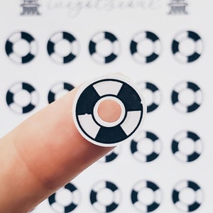 May include: A close-up of a black and white life preserver sticker. The sticker is round and has a white center with a black ring around it. The sticker is on a finger.
