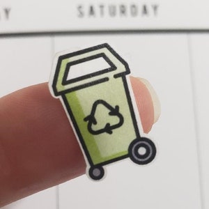 Könnte beinhalten: Grüner Recycling-Mülleimer-Aufkleber mit schwarzem Umriss und Rädern. Der Mülleimer hat ein Recycling-Symbol auf der Vorderseite.