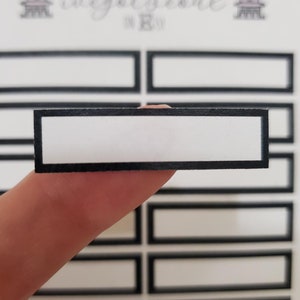 May include: A sheet of black and white rectangular labels with a white background and a black border. The labels are designed for writing on and are perfect for organizing and labeling.