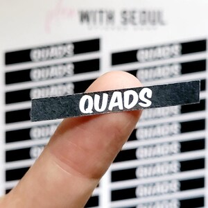 May include: A black and white sticker with the word "QUADS" printed in white bold letters.
