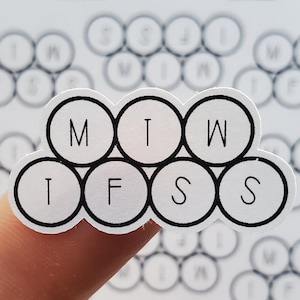 May include: A white sticker with black outlines and letters. The sticker is shaped like a honeycomb with six circles. The letters in the circles spell out "M T W T F S S".