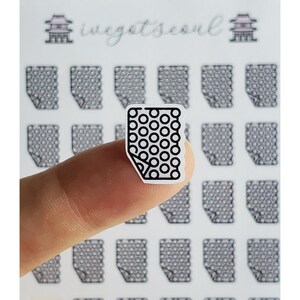 May include: A small, white sticker with a black outline and a pattern of black circles. The sticker is held by a finger, with other similar stickers in the background. The text "ivegotseoul" is visible in the background.