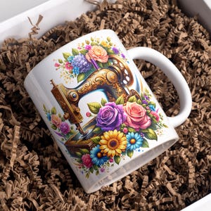 May include: A white ceramic mug featuring a detailed illustration of an ornate, vintage-style sewing machine surrounded by a vibrant arrangement of colorful flowers, including purple, pink, and yellow roses, along with blue and yellow daisies.