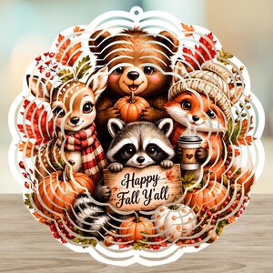 Op de afbeelding: Een ronde metalen windspinner met een kleurrijke herfstillustratie van een beer, een hert, een vos en een wasbeer, omringd door pompoenen en herfstbladeren. De wasbeer houdt een houten bordje vast met de tekst Happy Fall Y'ALL erop gedrukt.