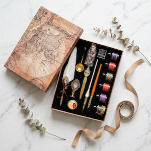 May include: A vintage calligraphy set in a decorative box. The box features a world map design. Inside, there are ink bottles, pens, a feather quill, and other writing accessories. The set includes a variety of colours and ornate details.
