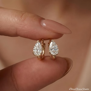 Peut inclure: Une paire de créoles en or avec une pierre précieuse transparente en forme de poire montée sur un serti clos. Les boucles d'oreilles présentent une finition métallique polie et un mécanisme de fermeture à charnière en forme de goutte.