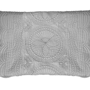 May include: A gray quilted pillow with a scalloped edge and a decorative floral pattern.