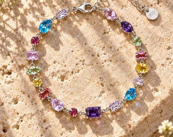 Op de afbeelding: Een armband van sterling zilver met een verscheidenheid aan veelkleurige edelstenen in verschillende vormen, waaronder peer-, ovaal- en rechthoekige slijpvormen. De ketting heeft een karabijnsluiting en een rond label met 925-stempel.