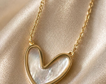 Op de afbeelding: Een goudkleurige ketting met een hartvormige hanger met een inleg van iriserend parelmoer. De hanger hangt aan een fijne goudkleurige ketting en is voorzien van een gladde, gepolijste metalen rand rondom het hartvormige midden.