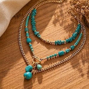 Può includere: Una collana a più fili con catene in metallo color oro e perline in pietra color turchese. Il design presenta una chiusura a T sul davanti con due ciondoli in pietra color turchese pendenti e piccole perline in metallo color oro.