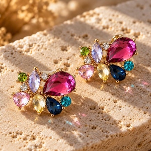 May include: A pair of gold-tone stud earrings featuring a cluster of multi-colored faceted crystals. Each earring includes a large teardrop-shaped magenta stone, accented by smaller round, oval, and pear-shaped crystals in pink, yellow, blue, green, and clear.