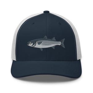 May include: A navy blue trucker hat with a white mesh back. The front panel features an embroidered striped fish design in shades of gray and white. The hat has a curved brim and a snapback closure.
