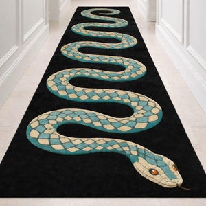 Peut inclure: Tapis de couloir noir avec un motif de serpent stylisé. Le corps du serpent est orné de losanges bleus et crème. La tête du serpent a des yeux orange et une petite langue fourchue.