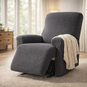 May include: A dark grey recliner chair with a woven pattern. A cream-coloured throw blanket is draped over the armrest. The chair is in a living room setting with a window and a wooden cabinet in the background.