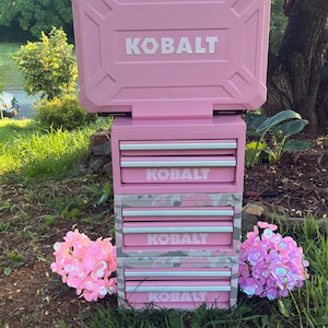 May include: A pink KOBALT tool chest with a top compartment and multiple drawers. The tool chest has a handle for carrying and the KOBALT logo is displayed in white. The drawers have a camouflage pattern.