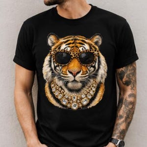 Könnte beinhalten: Ein schwarzes T-Shirt mit kurzen Ärmeln und einem Grafikdruck eines Tigergesichts, das eine Sonnenbrille mit Leopardenmuster sowie eine große, klobige goldfarbene Halskette mit klaren, facettierten Steinen trägt.