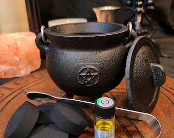 May include: A black cast iron cauldron with a pentagram symbol, a matching lid, and a metal handle. Included are four black charcoal discs, a pair of silver-toned metal tongs, and a small glass bottle containing yellow Grapes Oil.