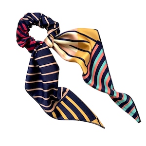 May include: A hair scrunchie with a long, flowing scarf tail. The scrunchie is dark red and black striped, while the scarf features a mix of navy, mustard yellow, coral pink, and teal stripes and geometric patterns. The scarf is tied in a bow around the scrunchie. This stylish hair accessory is perfect for adding a touch of elegance and flair to any outfit.