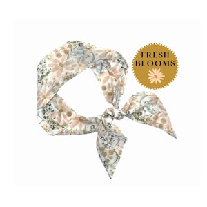 May include: A floral patterned headscarf with a tied knot. The scarf features a repeating pattern of beige flowers and green foliage on a white background. The text "FRESH BLOOMS" is in a gold circle.