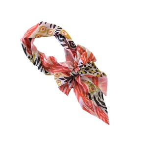 May include: A pink, white, and brown patterned silk scarf with a knotted design.