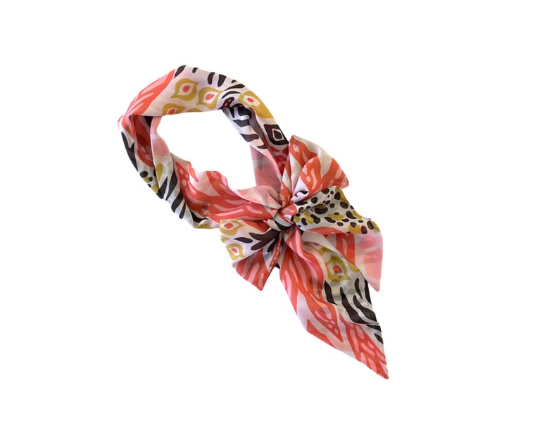 May include: A pink, white, and brown patterned silk scarf with a knotted design.